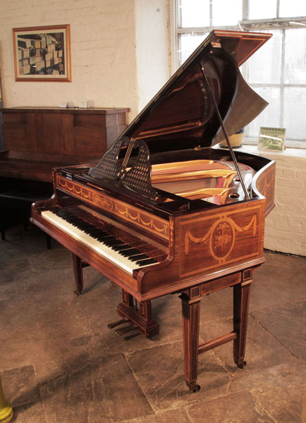 Pre-owned,  1903, Broadwood grand piano with a rosewood case and gate legs. Cabinet inlaid with swags, bows and panels of musical instruments. Piano has an eighty-five note keyboard and two-pedal lyre. 