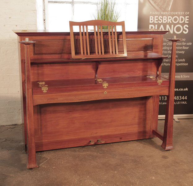 Arts and Crafts, 1899, Bechstein upright piano with a walnut case and large brass hinges. The large architectural candlesticks sit atop the square piano legs. Designed by Walter Cave. Piano has an eighty-five note keyboard and two pedals. 